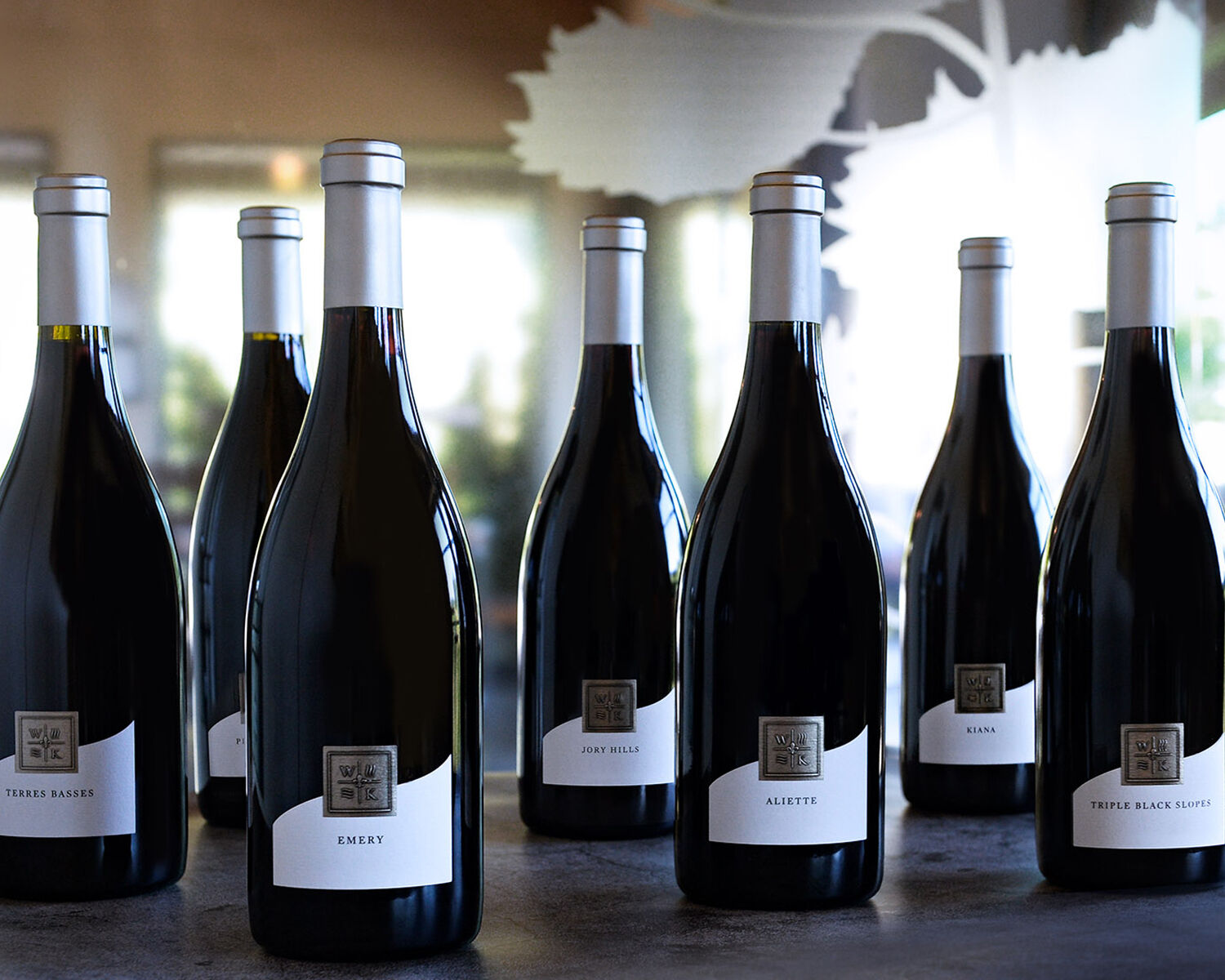 Seven bottles of WillaKenzie Estate Pinot Noir standing on a counter.